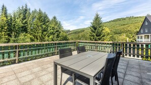 A patio with a table and chairs, surrounded by a wooden fence, overlooking a forested hillside. - Apartment 'Bödefeld' with Shared Terrace, Private Garden and Wi-Fi (Schmallenberg)
