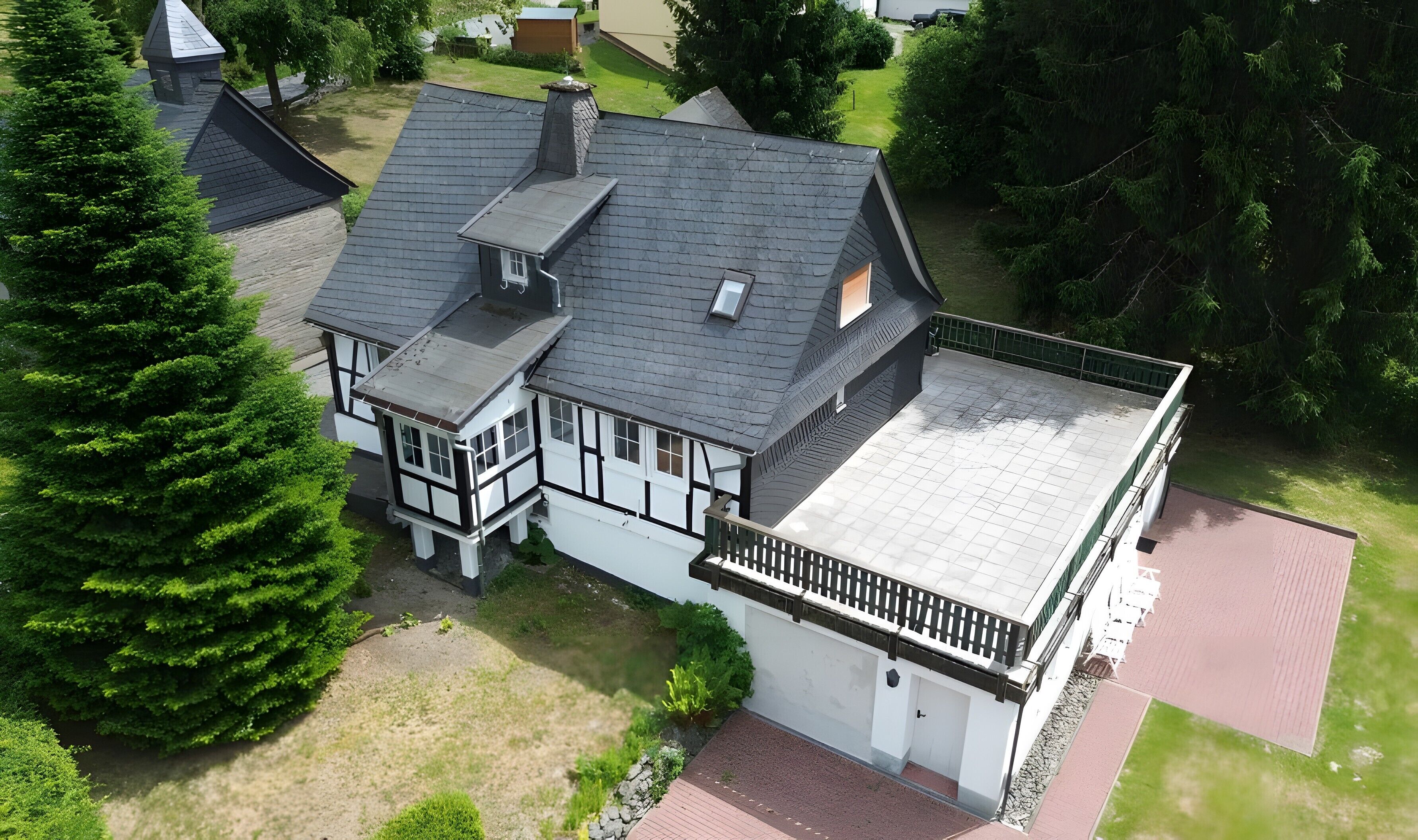 A two-story house with a sloped roof, a balcony, and a fenced yard.