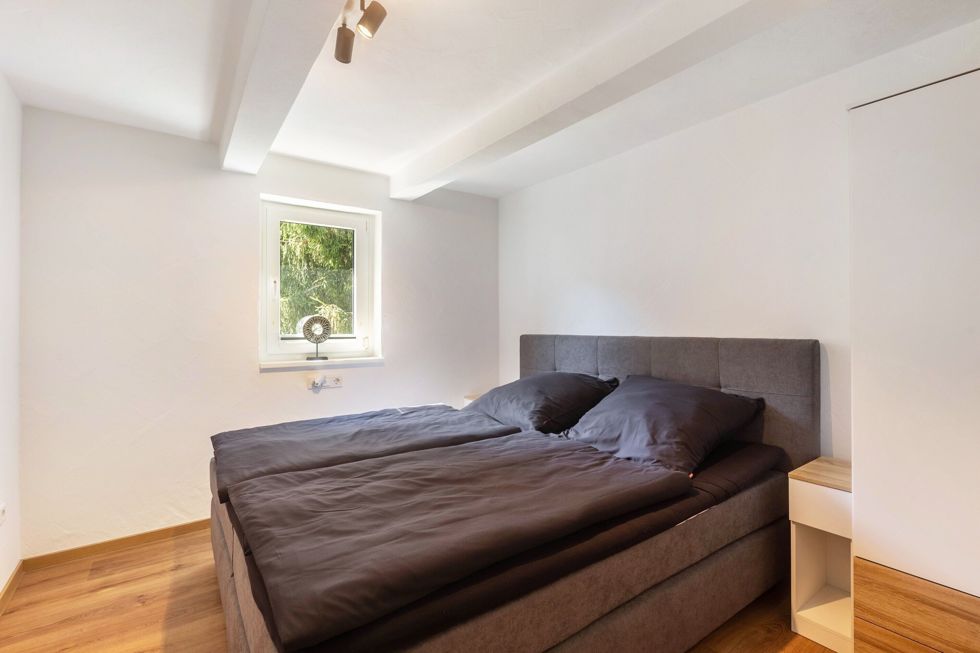 Ein Schlafzimmer mit Bett, Nachttisch, Fenster und Deckenventilator.