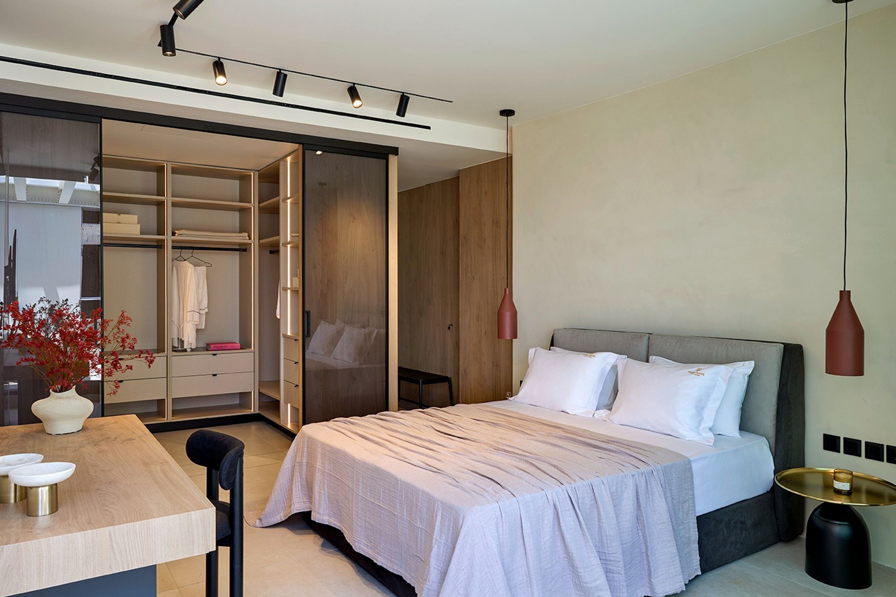 A modern hotel room with a large bed, a wooden wardrobe, a desk with a vase, and a pendant light.