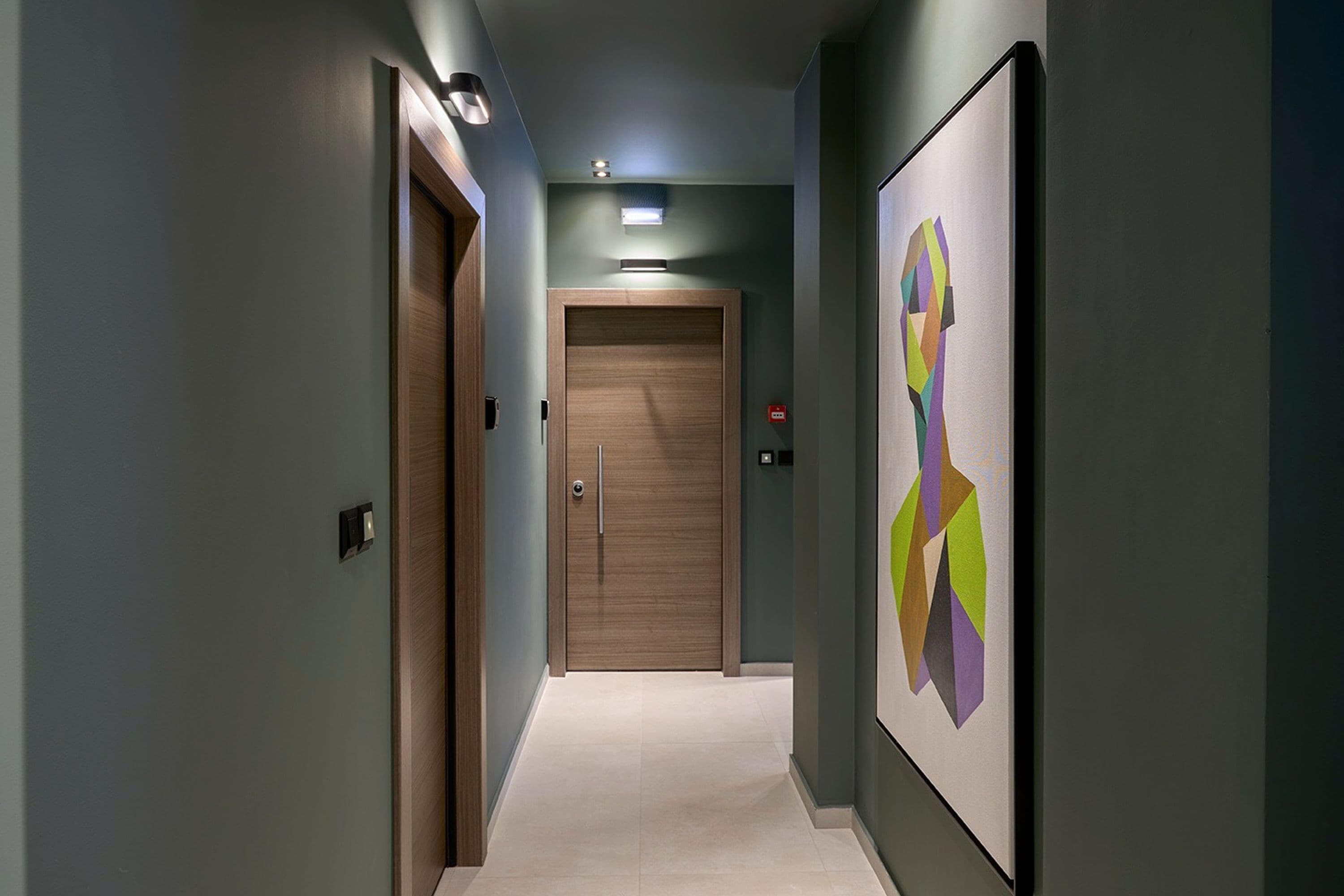 A hallway with a wooden door at the end, a light fixture above, and a colorful abstract painting on the wall.