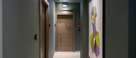 A hallway with a wooden door at the end, a light fixture above, and a colorful abstract painting on the wall.