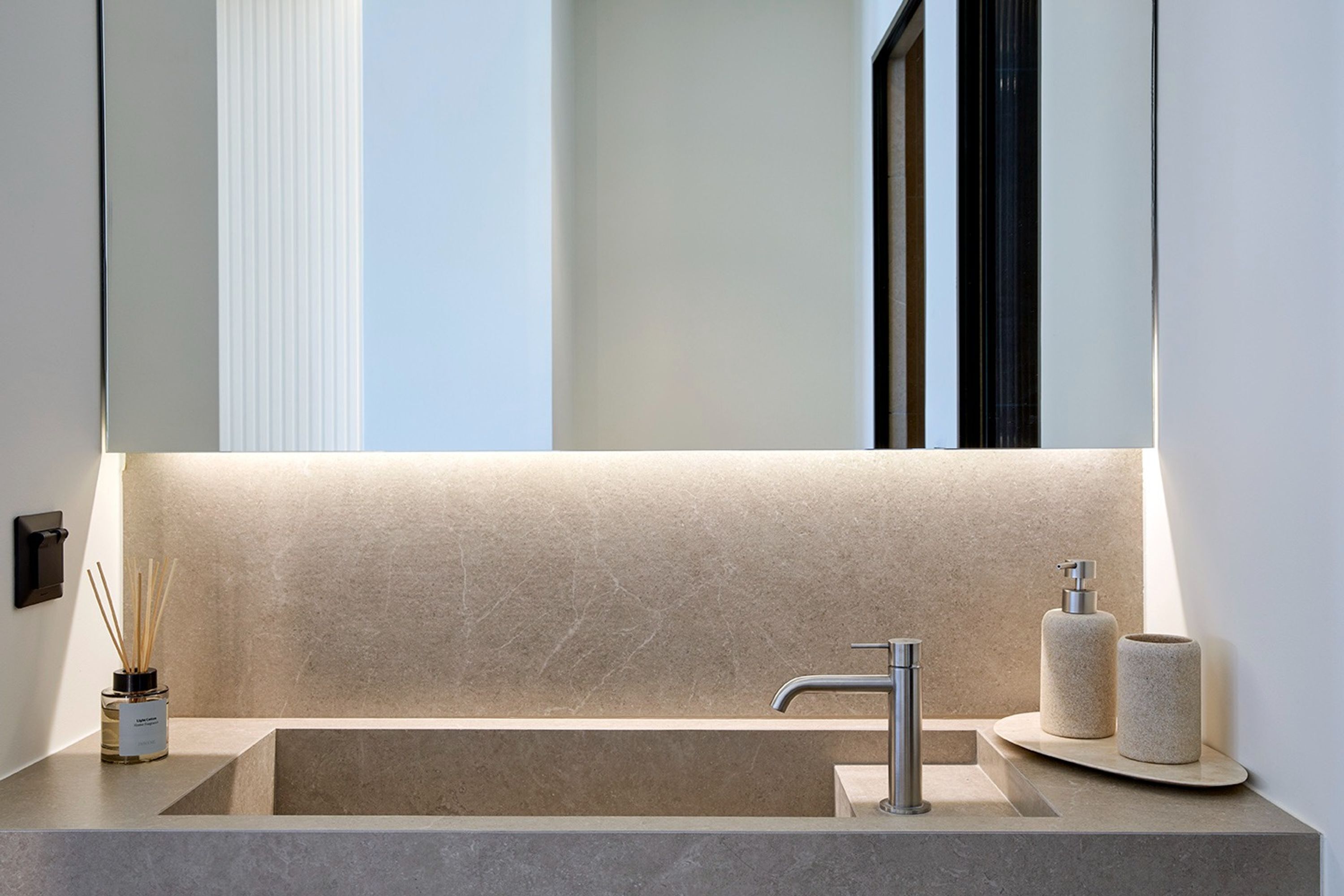 Un bagno moderno con un lavabo rettangolare, uno specchio grande e un dispenser di sapone a parete.