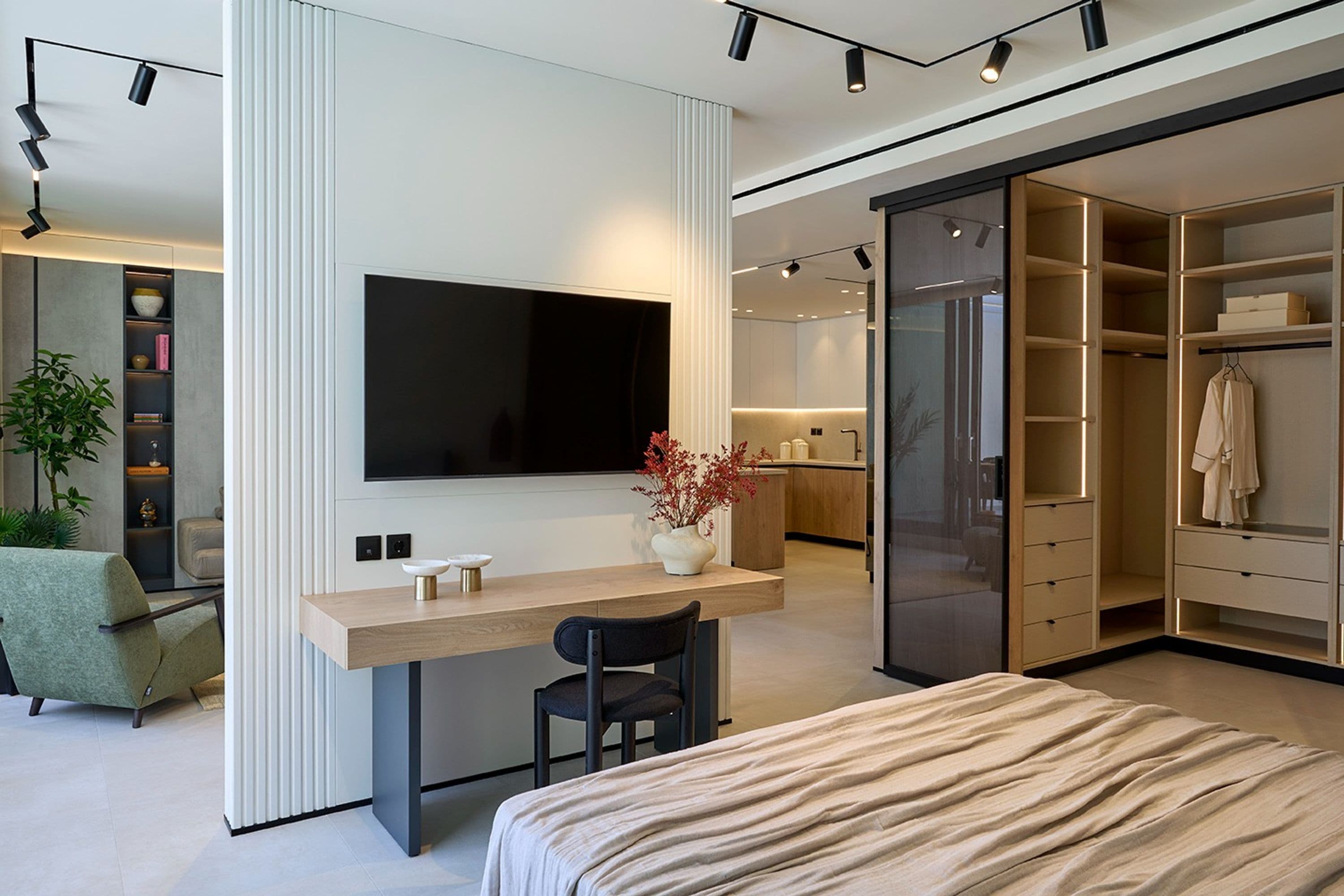 A modern bedroom with a large bed, a desk with a chair, a TV mounted on the wall, and a walk-in closet.