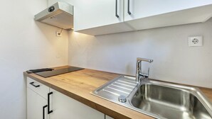 A kitchen with a stainless steel sink, wooden countertop, white cabinets, and a built-in range hood. - Apartment 'Gellinghausen' with Shared Terrace, Private Garden and Wi-Fi (Schmallenberg)