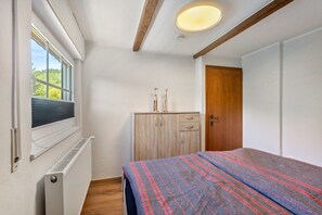 Ein Schlafzimmer mit einem Bett, einem Holzschrank, einem Heizkörper, einem Fenster mit Jalousien und einer Tür.