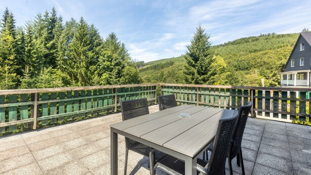A patio with a table and chairs, surrounded by a wooden fence, overlooking a forested hillside. - Apartment 'Gellinghausen' with Shared Terrace, Private Garden and Wi-Fi (Schmallenberg)