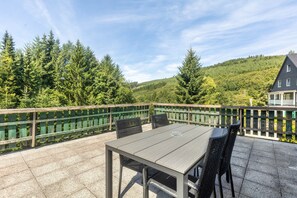 Eine Terrasse mit Tisch und Stühlen, umgeben von einem Holzzaun, mit Blick auf einen bewaldeten Hang.