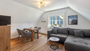 A modern loft with a dining area, a gray sofa, and a wooden table. - Apartment 'Gellinghausen' with Shared Terrace, Private Garden and Wi-Fi (Schmallenberg)