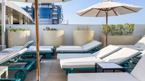 A rooftop lounge area with sunbeds, umbrellas, and potted plants. - LUX The Seven Res Palm Studio (Dubai)