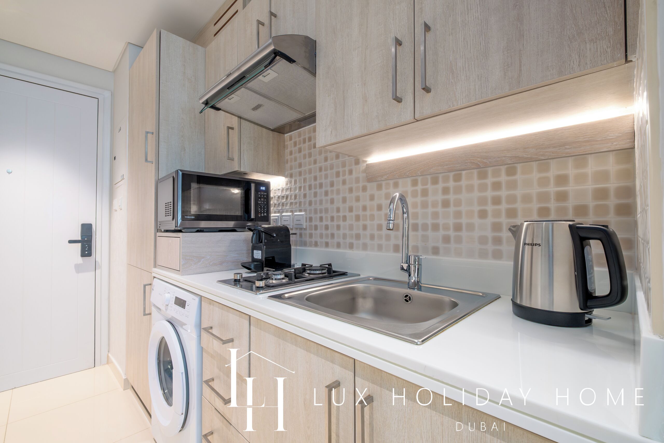 Een moderne keuken met een wasmachine, magnetron, spoelbak en waterkoker.