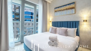 A hotel room with a large bed, a view of the city, and a balcony with a table and chairs. - LUX The Seven Res Palm Studio (Dubai)