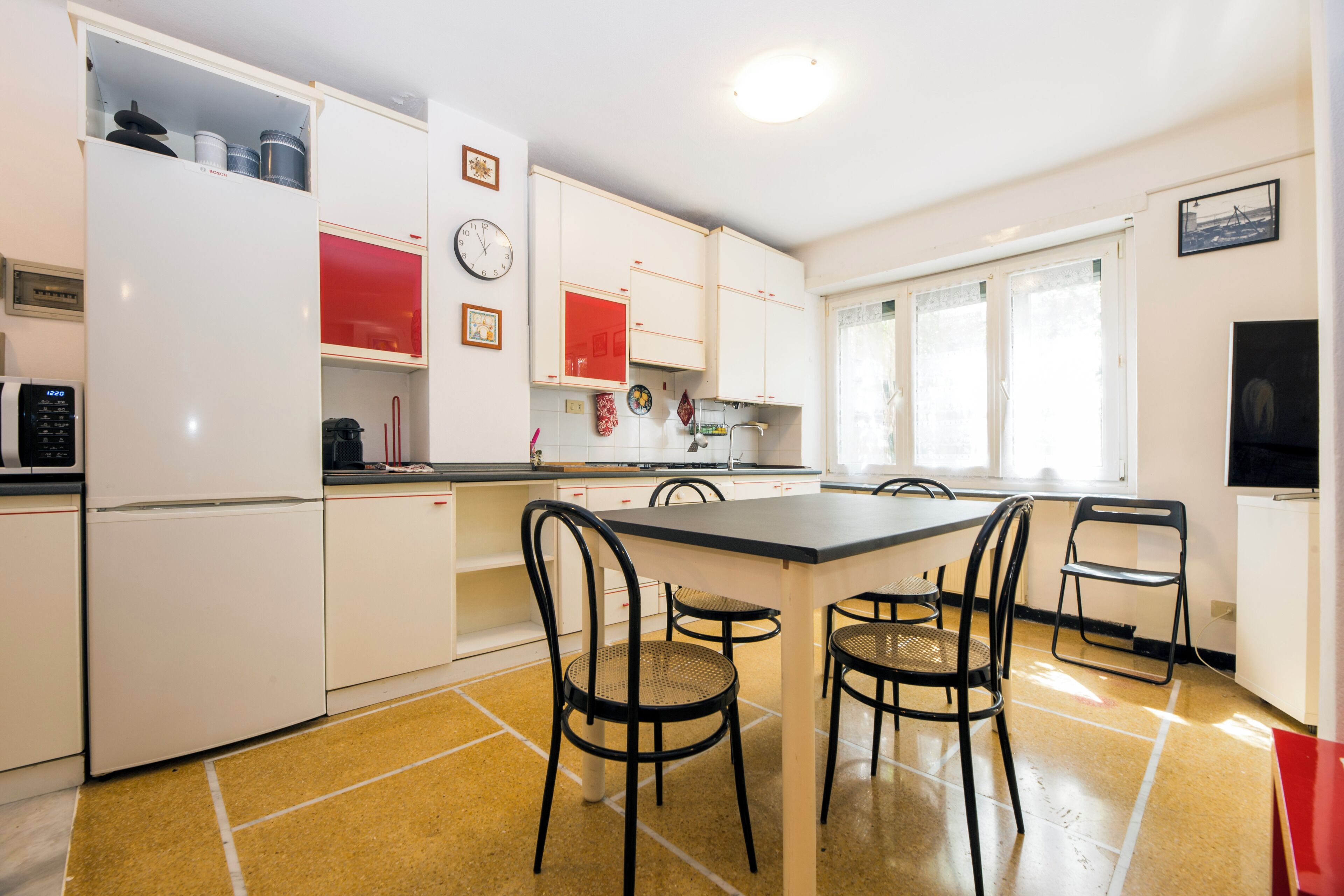 A kitchen with white cabinets, a red appliance, and a dining area with four chairs.