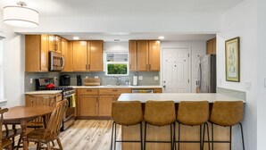 A modern kitchen with wooden cabinets, a stainless steel refrigerator, and a bar area with stools.