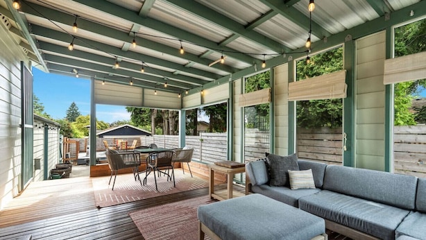 A covered outdoor living area with a wooden deck, a sofa, a dining table with chairs, and string lights.