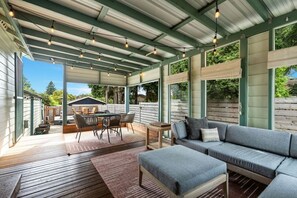 A covered outdoor living area with a wooden deck, a sofa, a dining table with chairs, and string lights.