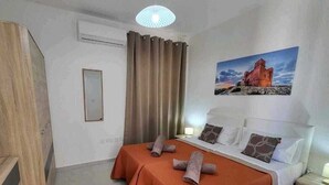 A hotel room with a bed, a nightstand, a mirror, a window with curtains, and a painting on the wall. - Unique Waterfront Penthouse: Lovely Sea Views - Spacious Balcony! (Il-Mellieħa)