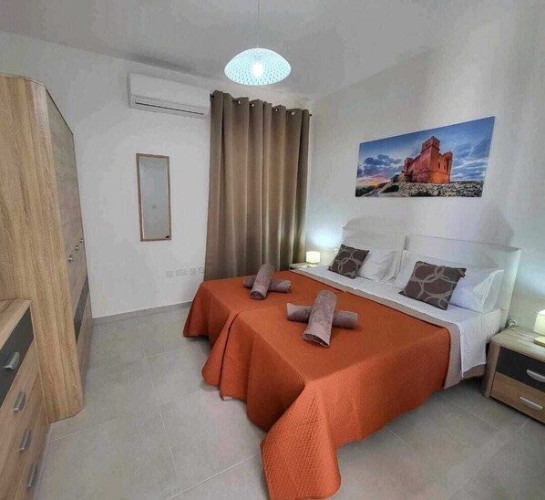 A hotel room with a bed, a nightstand, a mirror, a window with curtains, and a painting on the wall.