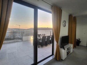 A balcony with a dining table and chairs, a TV on a stand, and curtains.
