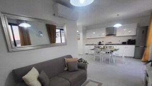 A modern living room with a sofa, a dining area with a table and chairs, and a kitchen with cabinets and appliances. - Unique Waterfront Penthouse: Lovely Sea Views - Spacious Balcony! (Il-Mellieħa)