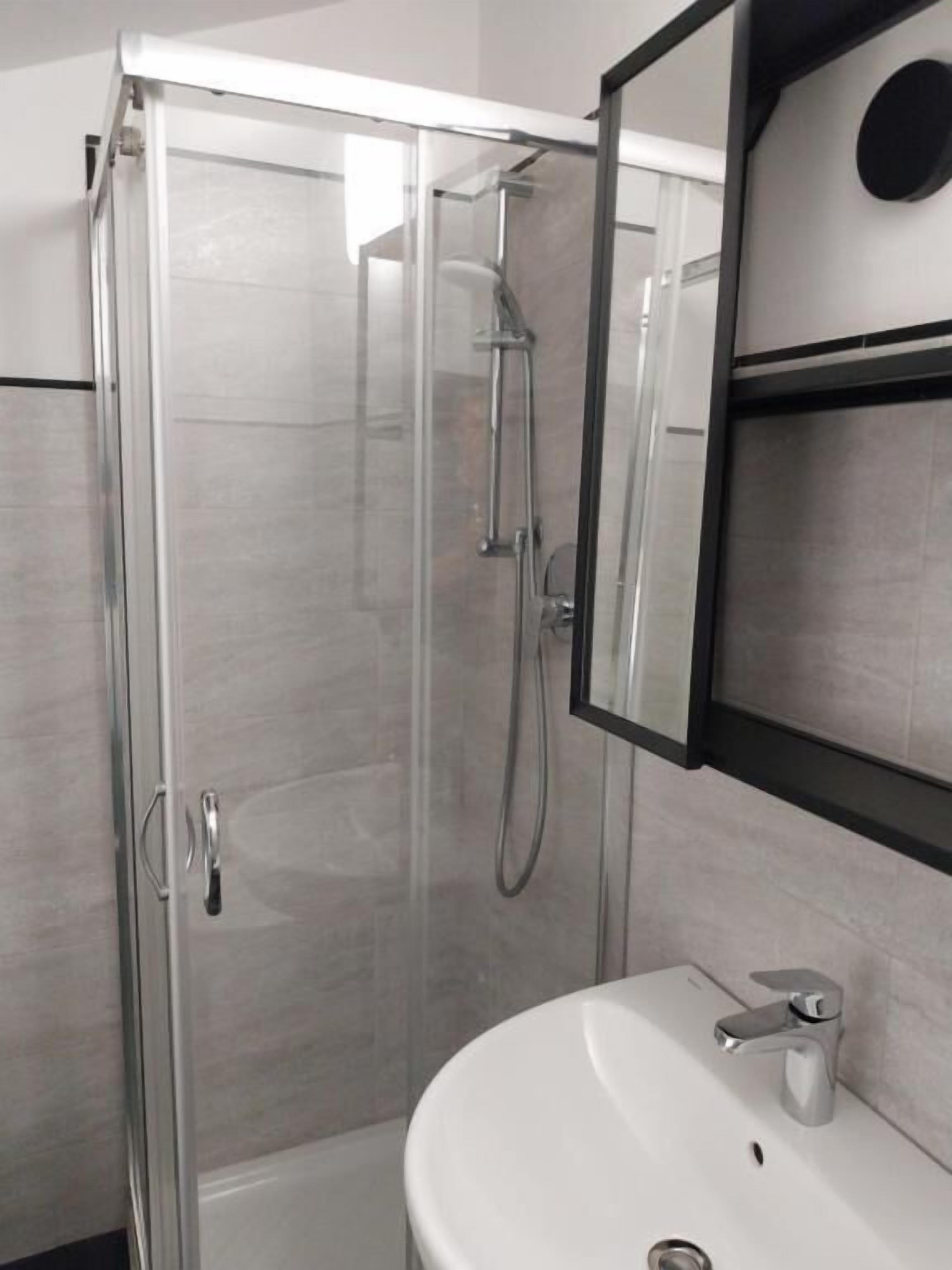 Uma casa de banho moderna com chuveiro envidraçado, lavatório branco e espelho em cima.