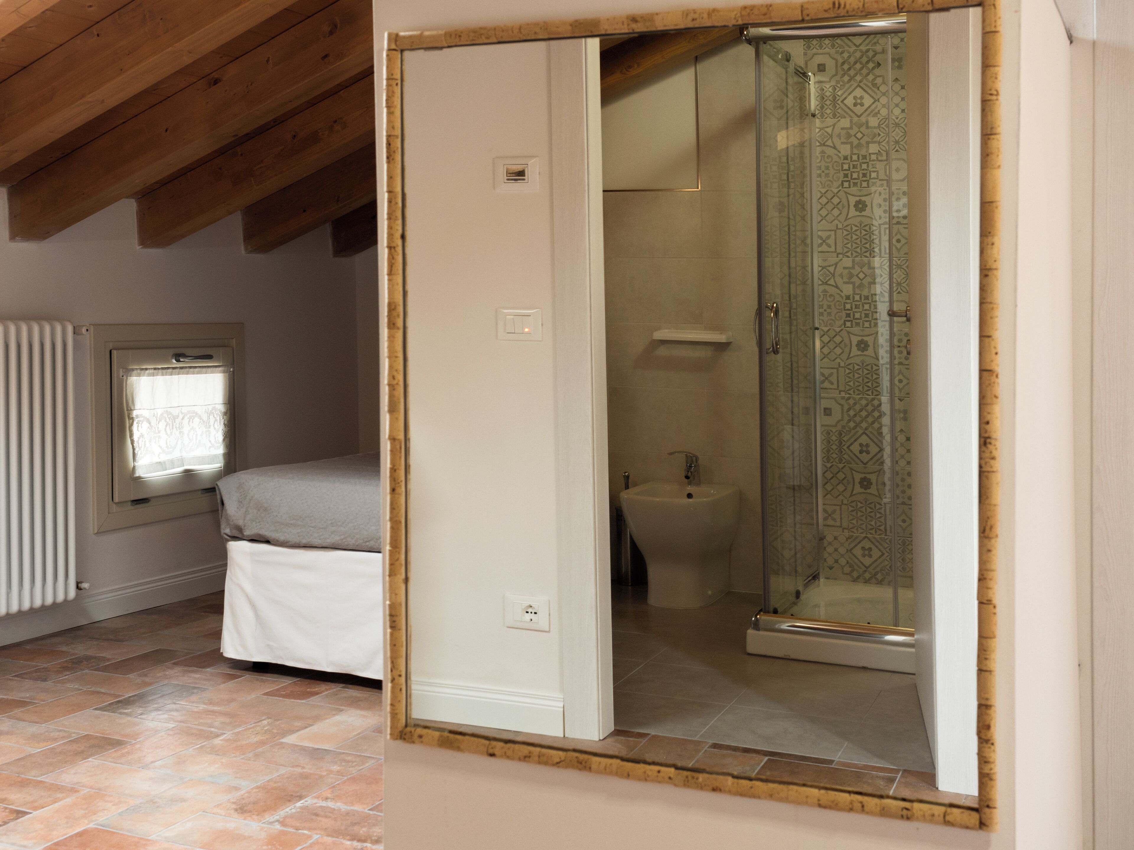 A bedroom with a bed, a window with curtains, a radiator, and a bathroom with a shower and toilet.