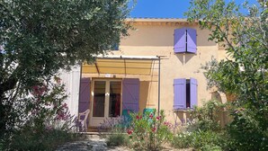 A building with a yellow facade, purple shutters, and a stone pathway leading to the entrance.