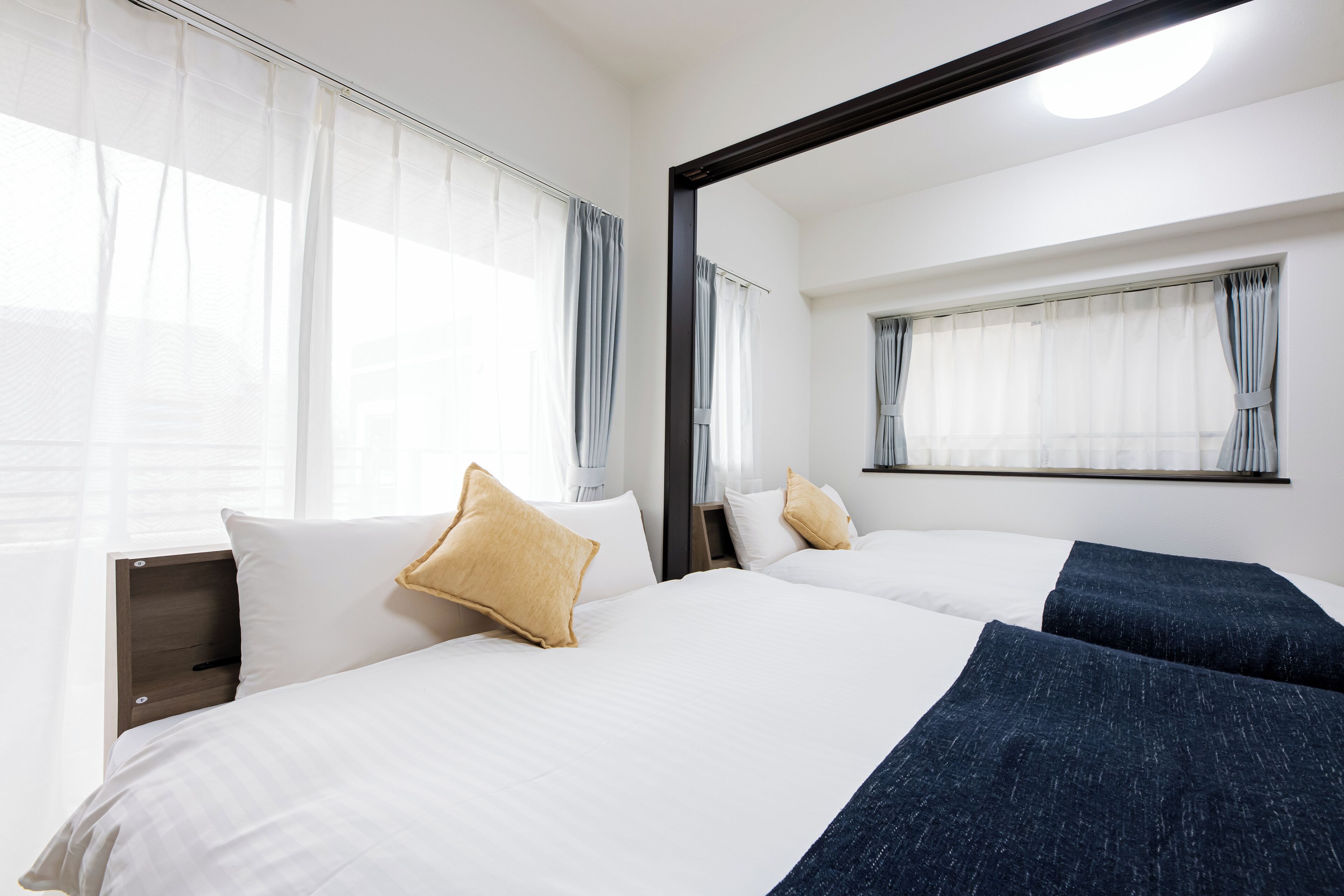 Habitación de hotel con dos camas, ropa de cama blanca y un espejo grande sobre ellas.