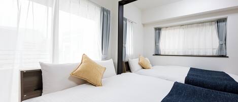 Habitación de hotel con dos camas, ropa de cama blanca y un espejo grande sobre ellas.