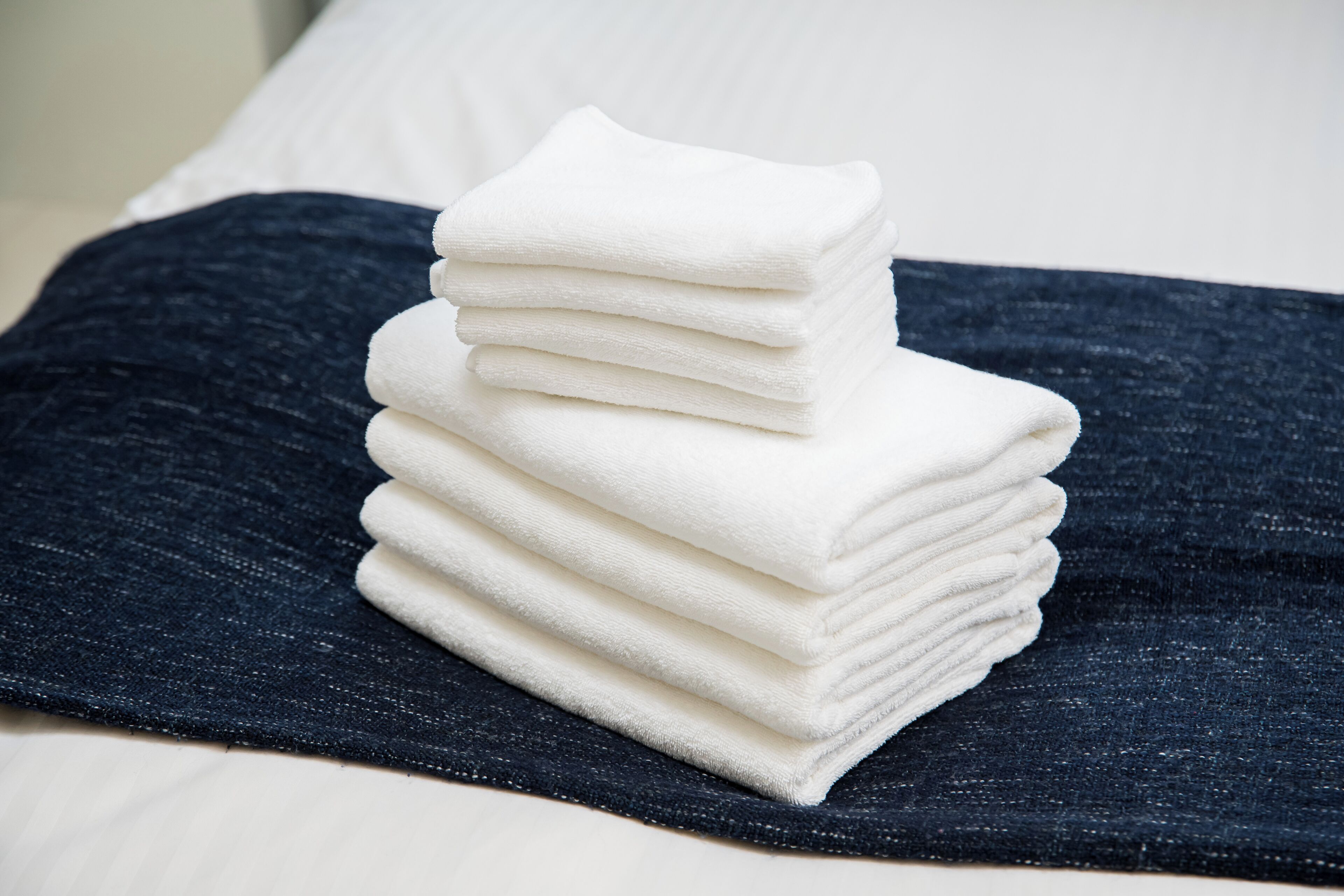 A stack of white towels on a dark blue bedspread.