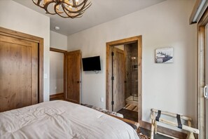 A bedroom with a large bed, wooden doors, a mounted TV, a shower, and a deer head artwork.