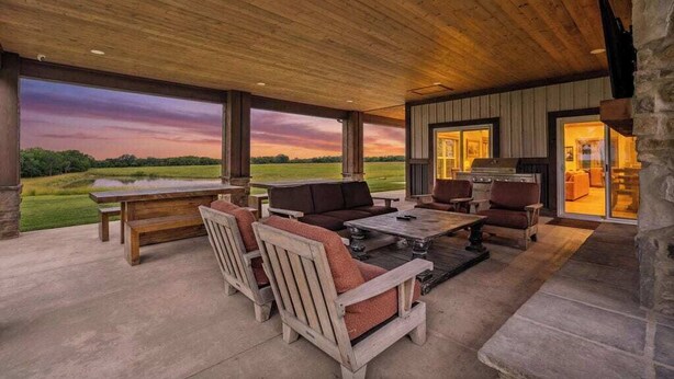 An outdoor patio area with a wooden ceiling, a large table, and seating.
