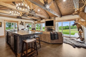 A spacious kitchen with a large island, bar stools, a fireplace, and a mounted deer head.