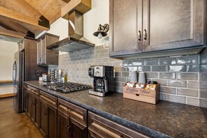 A kitchen with dark wood cabinets, a gas stove, a coffee maker, and a coffee bar sign.