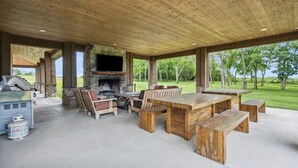An outdoor patio with a stone fireplace, wooden furniture, and a grill.