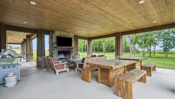 An outdoor patio with a stone fireplace, wooden furniture, and a grill.