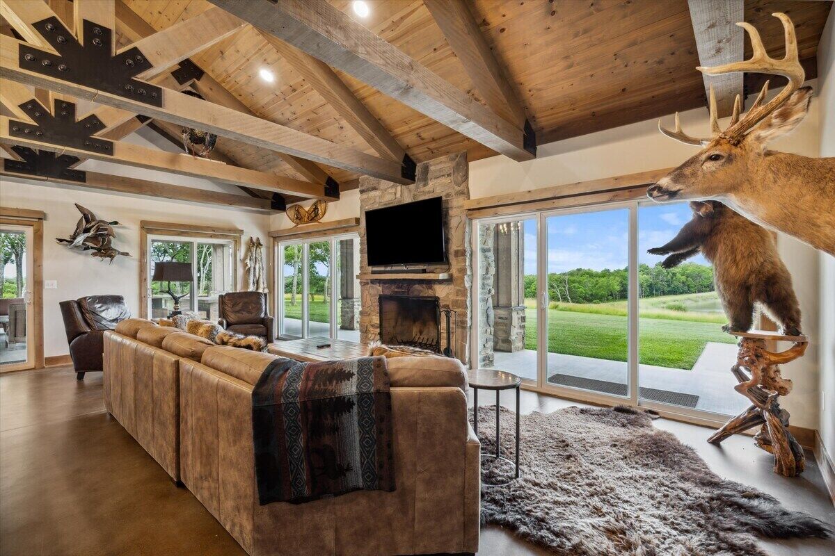 A spacious living room with a large fireplace, a mounted deer head, and a view of the outdoors.