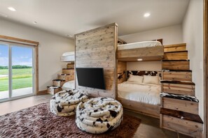 Ein Schlafzimmer mit Etagenbett, einem an einer Holzwand befestigten Fernseher und einem großen Fenster mit Blick auf eine grüne Landschaft.