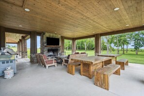 Eine Terrassengruppe im Freien mit Kamin aus Stein, Holzmöbeln und einem großen Fernsehbildschirm.