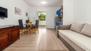 A compact living space with a wooden dining table, chairs, a sofa, a TV, and a kitchenette.