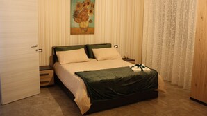 A bedroom with a bed, a nightstand, a drawer, a painting on the wall, and a door.