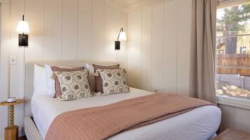 A bedroom with a large bed, two wall-mounted lamps, a bedside table, and a window with curtains.