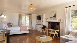 A cozy, well-lit living room with a bed, seating area, and a fireplace. - Charming Carmel Cottage Ocean & Mntn View Walk DT (Carmel)