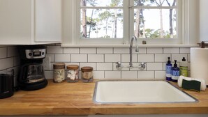 A kitchen with a white sink, a coffee maker, and jars of coffee and spices. - Charming Carmel Cottage Ocean & Mntn View Walk DT (Carmel)