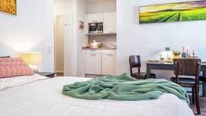 Una habitación de hotel con una cama, una manta verde, un escritorio con una silla, una zona de cocina y un cuadro en la pared.