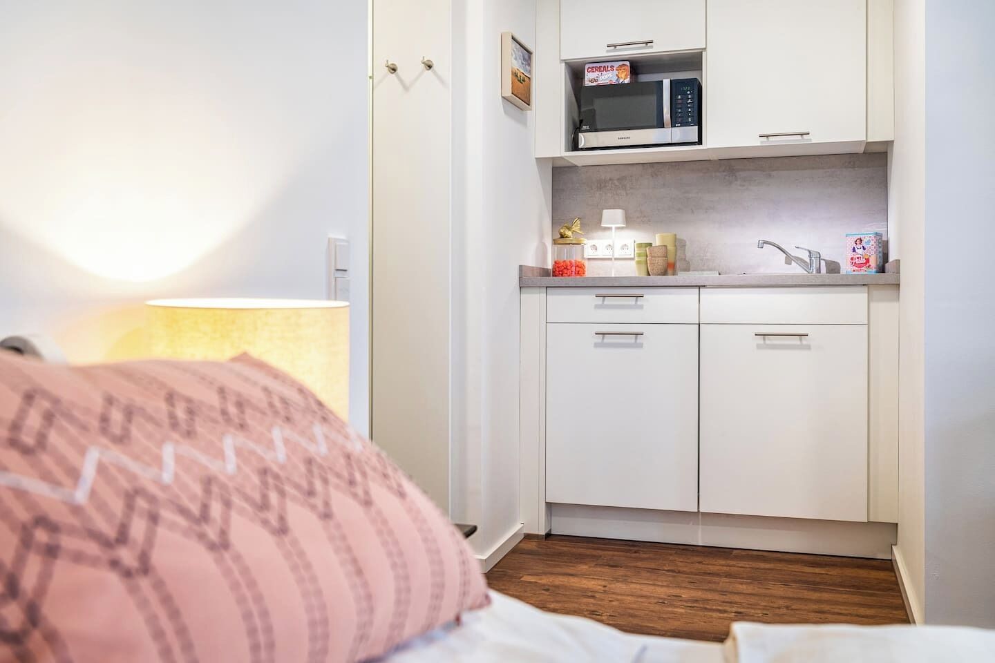 Una cocina compacta con gabinetes blancos, un microondas y un lavabo.