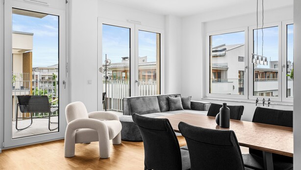 Un comedor moderno con una mesa de madera, sillas blancas y negras, y vistas al balcón exterior.