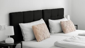 Una cama bien hecha con almohadas blancas y beige, un cabecero tapizado en negro y una mesita de noche con lámpara.