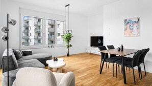 Una sala de estar moderna con un sofá, una mesa de comedor con sillas, un televisor y un ventanal con vistas a edificios.