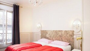 A hotel room with a bed, a nightstand, a chandelier, and a window with curtains. - Practical Apartment for 3 people in charming Paris (Paris)